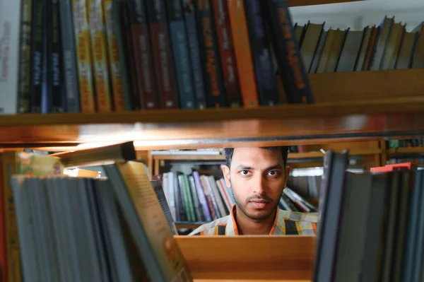 Stock image Portrait of cheerful male international Indian student with backpack, learning accessories standing near bookshelves at university library or book store during break between lessons. Education concept.