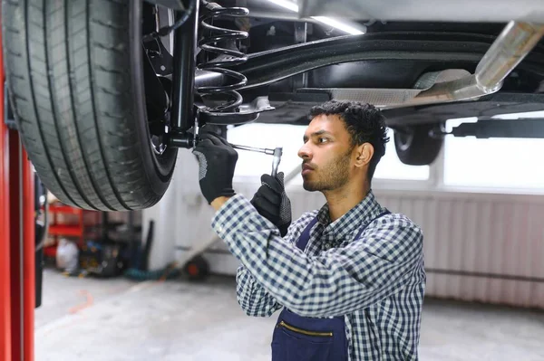 stock image latin hispanic auto mechanic in uniform is examining a car while working in auto service.