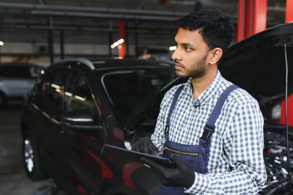 インドの自動車整備士は サービスステーションに立って働いています 解除された車を調べる車の専門家 青い色の整備士の制服を着たプロの修理工 — ストック写真