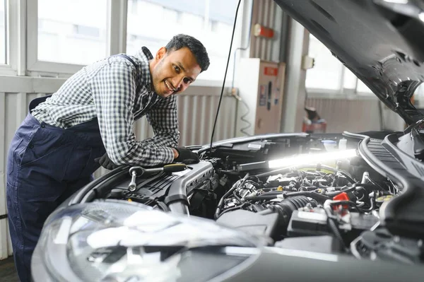 他那穿着制服的惊慌的汽车修理工在为汽车服务时正在检查汽车 — 图库照片