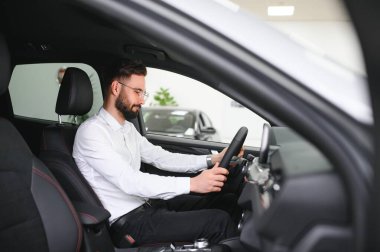 Happy caucasian man in formal wear getting inside luxury modern car for testing interior before purchase. Concept of dealership, selling and purchase.