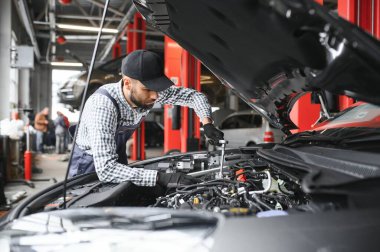 Mavi üniformalı yetişkin adam otomobil salonunda çalışıyor.