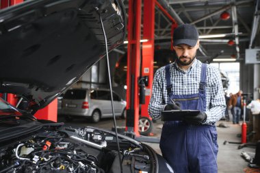 Araç motorunun yanında duran ve kaputu açık arızayı tespit eden profesyonel beyaz araba tamircisi..