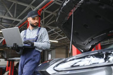 Mavi üniformalı yetişkin adam otomobil salonunda çalışıyor.