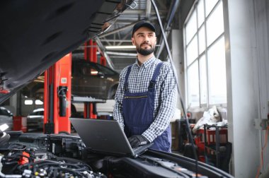 Gülümseyen tamirci tamirhanede dizüstü bilgisayar kullanıyor.