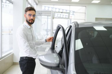 Happy caucasian man in formal wear getting inside luxury modern car for testing interior before purchase. Concept of dealership, selling and purchase.