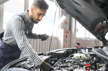 Mavi üniformalı yetişkin adam otomobil salonunda çalışıyor.