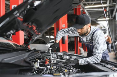 Profesyonel tamirci araba servisinde bir araba üzerinde çalışıyor. Güvenlik Gözlüklü Tamirci bir aracın motorunu tamir ediyor. Uzman bir Ratchet ile vidaları söküyor. Modern Temiz Atölye.