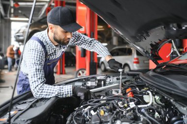 Profesyonel tamirci araba servisinde bir araba üzerinde çalışıyor. Güvenlik Gözlüklü Tamirci bir aracın motorunu tamir ediyor. Uzman bir Ratchet ile vidaları söküyor. Modern Temiz Atölye.