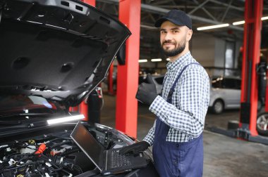 Yakışıklı araba tamircisi araba servisinde poz veriyor.