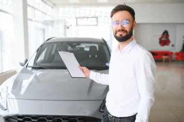 Kendine güvenen Kafkasyalı genç işadamı araba galerisinde duruyor..