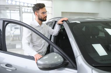 Happy caucasian man in formal wear getting inside luxury modern car for testing interior before purchase. Concept of dealership, selling and purchase.