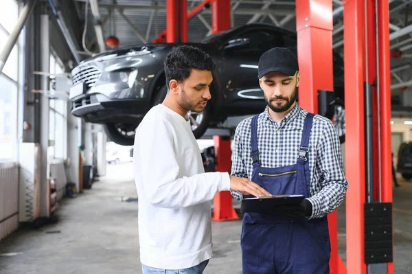 A mechanic in a car service is talking to an Indian car owner. Car service concept