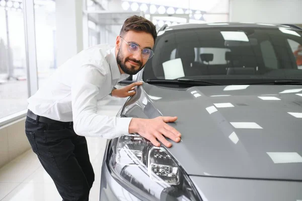 幸せな若い男は新しい高級車をチェックし ディーラーセンターで自動車を購入します 陽気な千年紀の白人男性の肖像ショールーム店で自動車を検討 — ストック写真