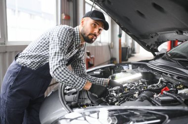 Yakışıklı araba tamircisi araba servisinde poz veriyor.