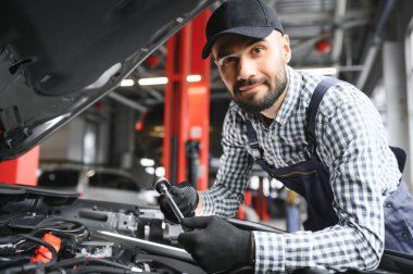 Yakışıklı araba tamircisi araba servisinde poz veriyor.