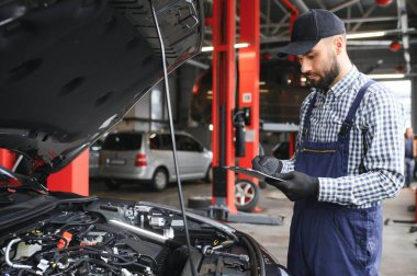 Araç motorunun yanında duran ve kaputu açık arızayı tespit eden profesyonel beyaz araba tamircisi..