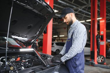 Mavi üniformalı yetişkin adam otomobil salonunda çalışıyor.