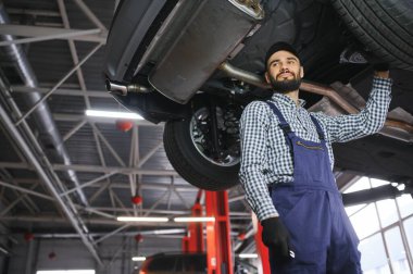 Mavi üniformalı yetişkin adam otomobil salonunda çalışıyor.