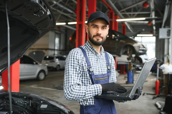 Smiling mechanic using a laptop pc at the repair garage