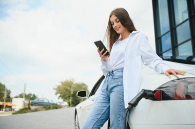 Elektrikli araba caddede şarj oluyor. Ekolojik Araba Bağlı ve Şarj Bataryaları. Bekleyen Kız Elektrik Aracına Yükleme İçin Bağlandı