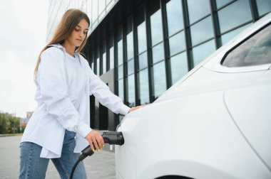 Elektrikli arabanın yanındaki kadın. Araç şarj istasyonunda yüklendi.