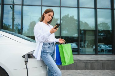 Elektrikli arabanın yanındaki kadın. Araç şarj istasyonunda yüklendi.