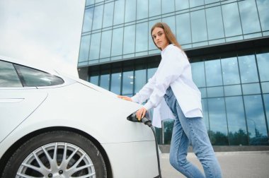 Kız elektrik benzinliğinde elektro araba şarj ediyor..