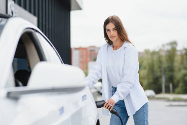 Elektrikli arabanın yanındaki kadın. Araç şarj istasyonunda yüklendi.
