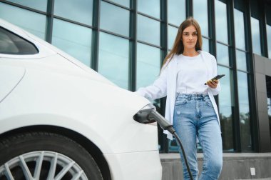 Kız elektrik benzinliğinde elektro araba şarj ediyor..