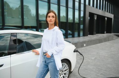 Elektrikli arabanın yanındaki kadın. Araç şarj istasyonunda yüklendi.