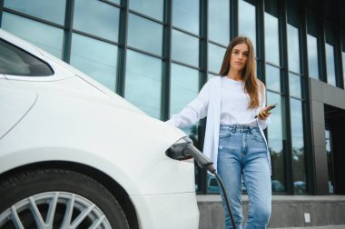 Elektrikli araba caddede şarj oluyor. Ekolojik Araba Bağlı ve Şarj Bataryaları. Bekleyen Kız Elektrik Aracına Yükleme İçin Bağlandı