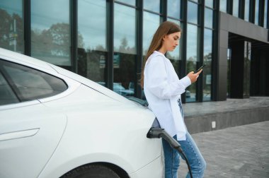 Kız elektrik benzinliğinde elektro araba şarj ediyor..