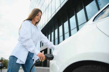 Elektrikli arabanın yanındaki kadın. Araç şarj istasyonunda yüklendi.