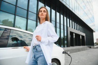 Elektrikli araba caddede şarj oluyor. Ekolojik Araba Bağlı ve Şarj Bataryaları. Bekleyen Kız Elektrik Aracına Yükleme İçin Bağlandı