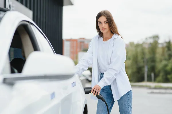 女の子の手は白い車の背景に電気自動車を充電するためのケーブルを保持しています — ストック写真