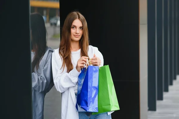 woman holding shopping bags of luxury brands, walking near shopping mall.