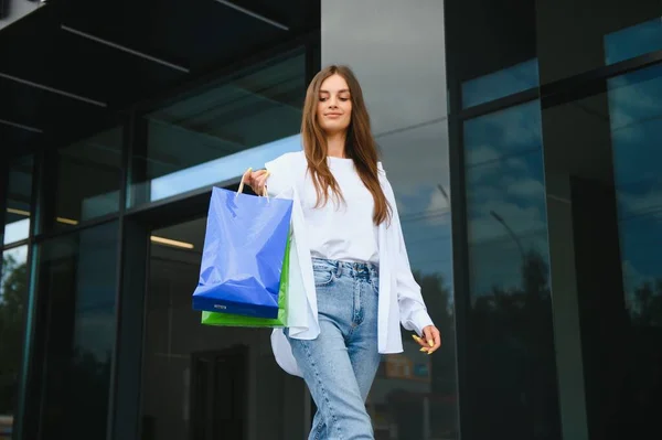 屋外の店の近くのショッピング バッグと美しい若い女性 — ストック写真