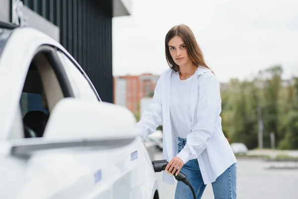 Stock image Woman near electric car. Vehicle charged at the charging station