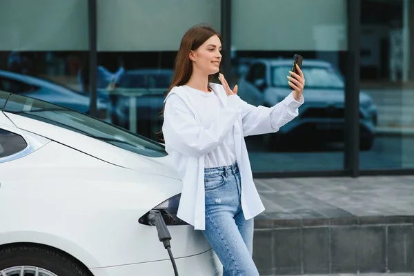 Telefon Ellerinde Elektrikli Arabalardaki Kadın Gündüz Şarj Istasyonunda Yepyeni Bir — Stok fotoğraf