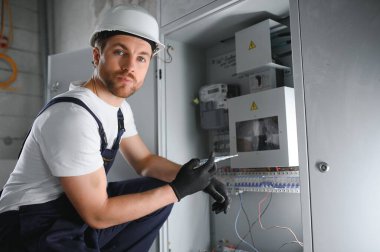 Elektrik santralinde fitillerle çalışan bir elektrik teknisyeni. Elektrik ekipmanlarının kurulumu ve bağlantısı. Elindeki aletlerle profesyonelce. kompleks çalışma konsepti, metin için alan