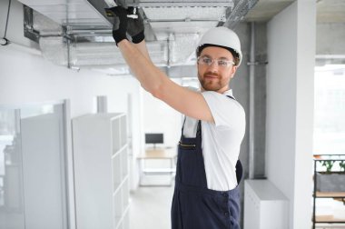 40 'lı yaşlarındaki beyaz tenli teknisyen yeni yeni kurulmuş depo havalandırma sistemini test ediyor. Ticari Isıtma, Soğutma ve Havalandırma Sistemleri.