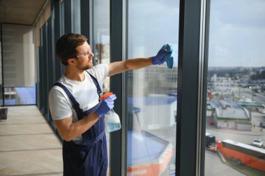 Erkek profesyonel temizlik işçisi özel ekipmanlı bir mağazanın camlarını ve pencerelerini temizliyor.