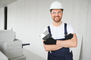 Üniformalı genç bir ustabaşının portresi bir binanın içinde, merdivenin yanında duruyor.