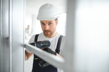 İnşaat işçisi iç bölme duvarı için metal profil yerleştirirken, arkasından bakıldığında yeni bir ev veya yenileme süreci inşa ediyor