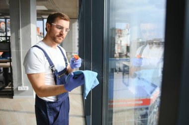 Erkek profesyonel temizlik işçisi özel ekipmanlı bir mağazanın camlarını ve pencerelerini temizliyor.