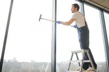 Erkek profesyonel temizlik işçisi özel ekipmanlı bir mağazanın camlarını ve pencerelerini temizliyor.