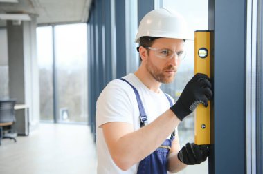 Worker using bubble level after plastic window installation indoors.