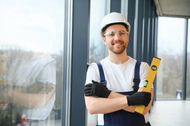 Yakışıklı genç adam yeni ev şantiyesine pencere takıyor.