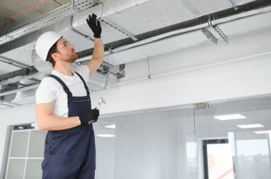 40 'lı yaşlarındaki beyaz tenli teknisyen yeni yeni kurulmuş depo havalandırma sistemini test ediyor. Ticari Isıtma, Soğutma ve Havalandırma Sistemleri.